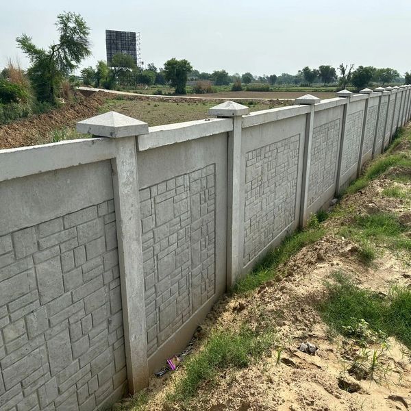 Long concrete fence with decorative patterns enclosing a green field.