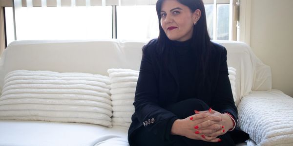 Woman sitting on white couch with folded hands.