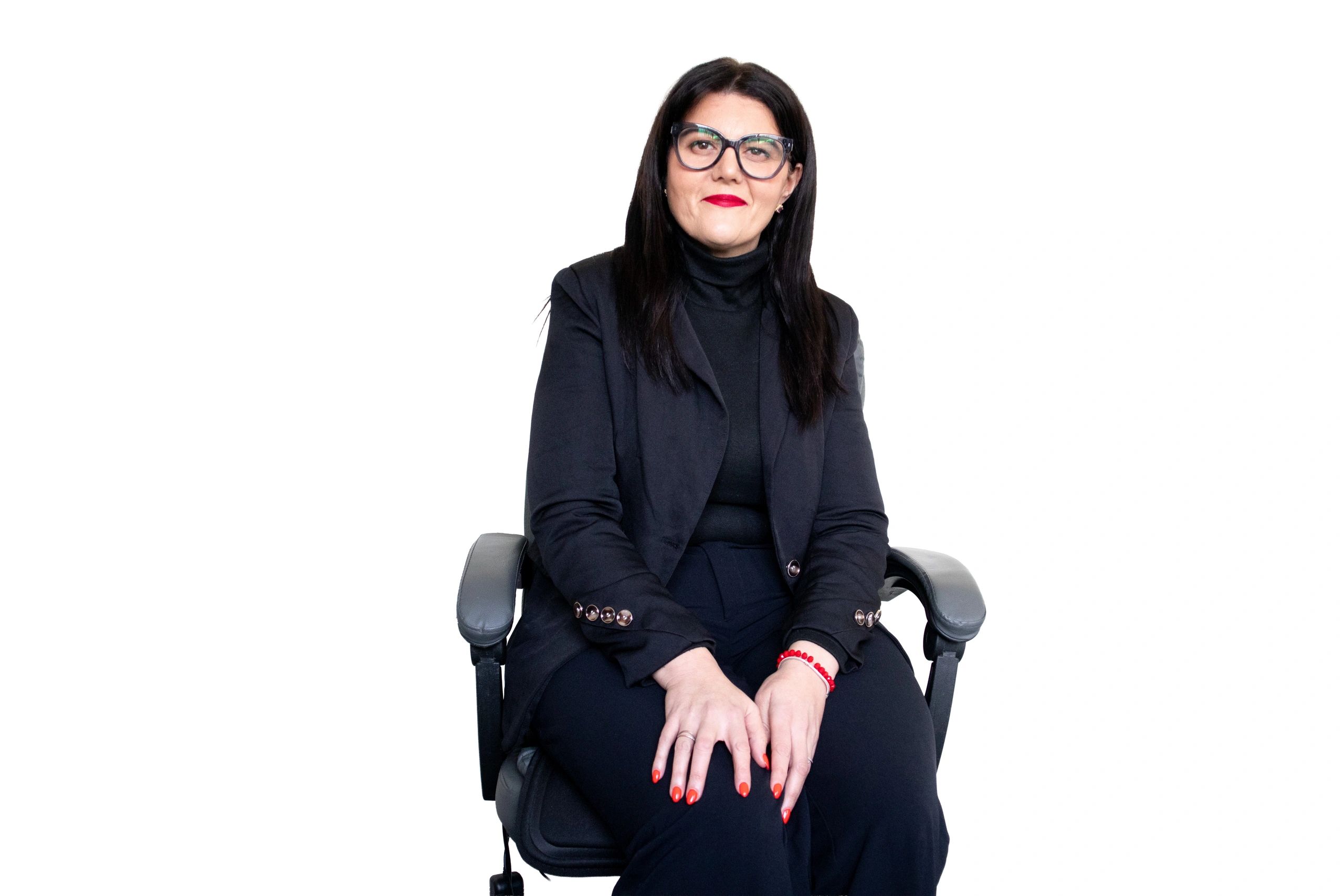 Woman sitting confidently in a chair with glasses and red lipstick.