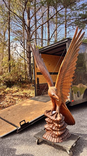 Intricately carved wooden eagle sculpture with wings spread, displayed outdoors near a trailer.