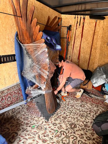 Man securing a large wooden eagle sculpture in a storage space.