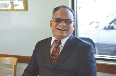 Ollie Cantos wearing a black suit and red tie smiling.