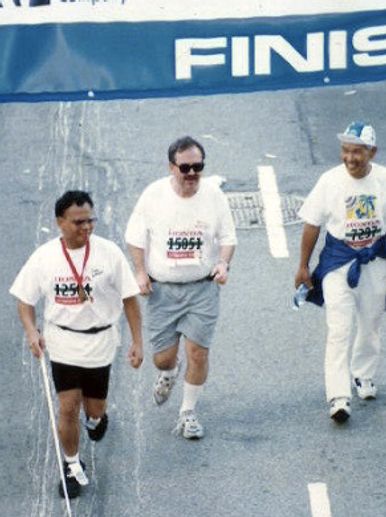 Ollie in a white T-shirt and black shorts wearing a number, crosses the marathon finish line.