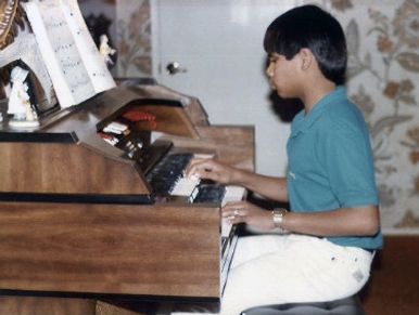 Ollie in a green polo and white pants plays the organ as a teenager.