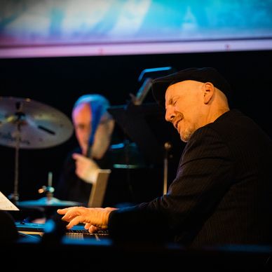 Sonny Barbato playing piano on stage, Todd Baker (right) and Dave Mattacks in background.