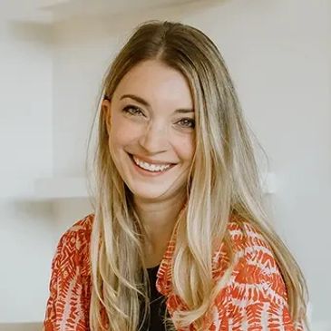 Smiling woman with long blonde hair wearing an orange patterned shirt.