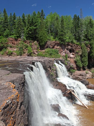 Waterfalls cascading over rocky cliffs surrounded by lush green forest.