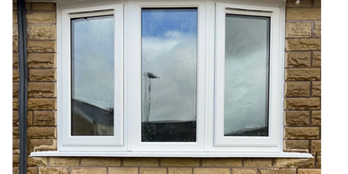 White framed bay window in a brick wall with rain droplets on glass.