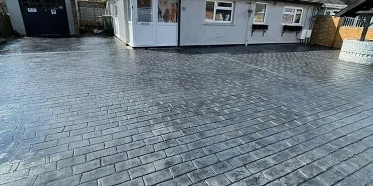Freshly paved driveway with a brick pattern in front of a house and garage.