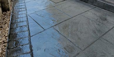 Wet concrete slabs with a textured border beside gravel.