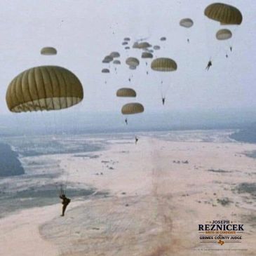 Military parachutes descending over a barren landscape.