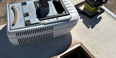 An RV roof with a removed air conditioner unit and a vacuum cleaner nearby.