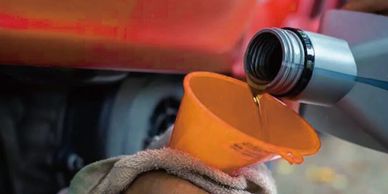 Pouring motor oil into an orange funnel held by a hand with a cloth.