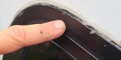Finger pointing at damaged seal on a vehicle window.