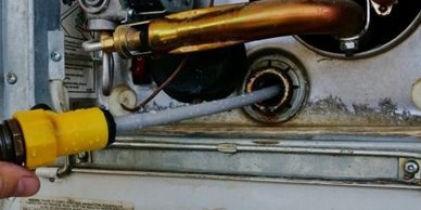 Hand holding a yellow-handled tool near pipes in a mechanical device.