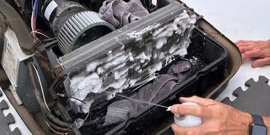 Person spraying foam cleaner on an air conditioning unit's evaporator coil.