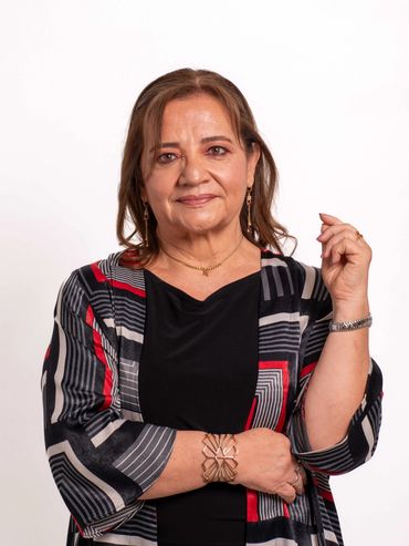 Mature woman with a confident smile wearing a patterned jacket and gold jewelry.