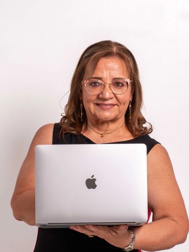 Smiling woman holding a silver MacBook laptop against a plain background.