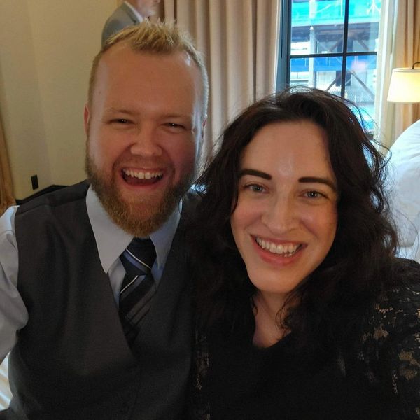 Smiling couple taking a cheerful selfie indoors near a window.