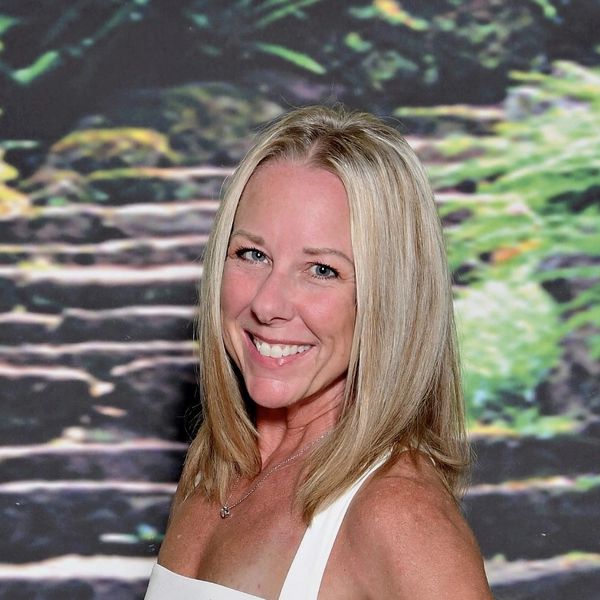 Smiling blonde woman posing in front of nature backdrop.