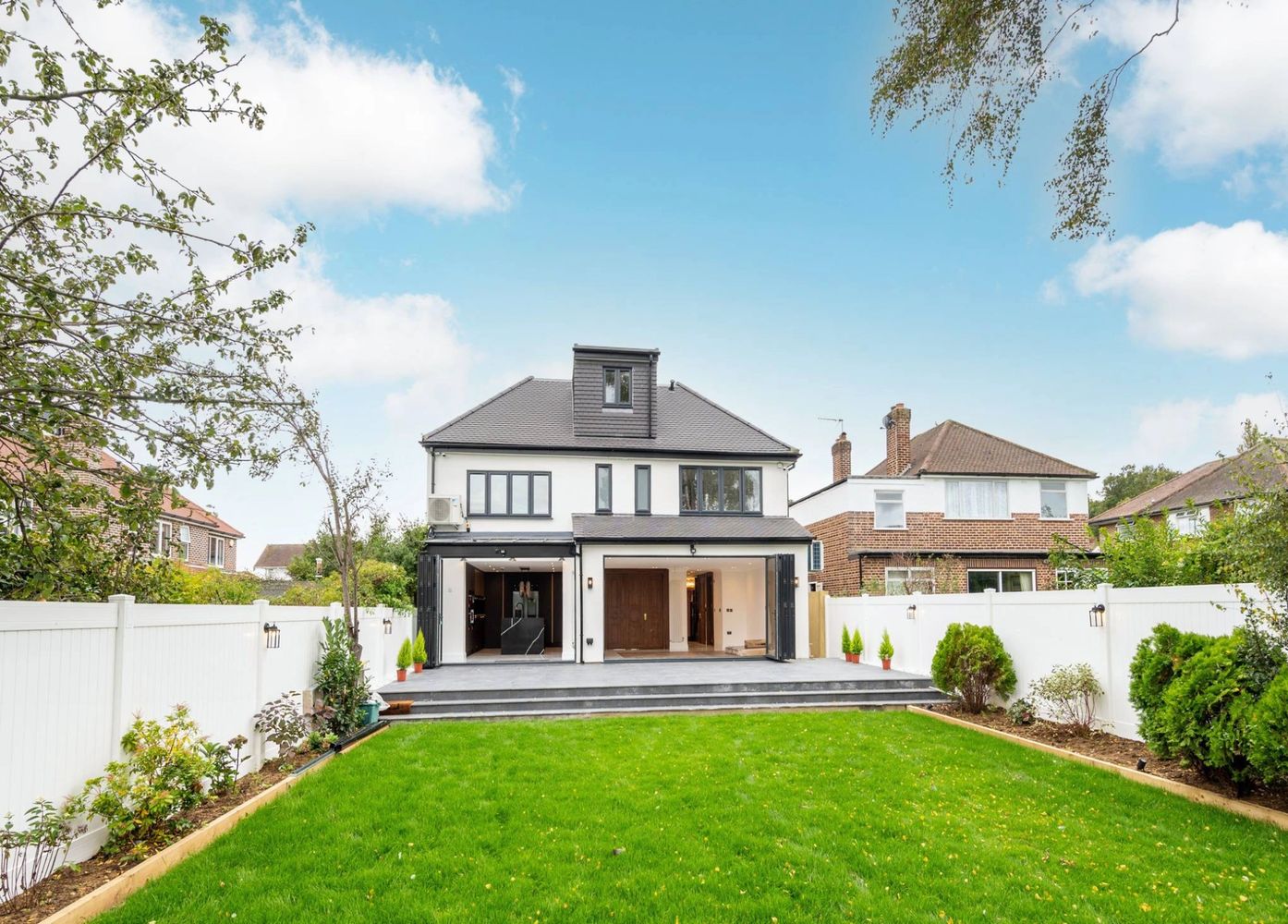 Modern two-story house with large glass doors opening to a spacious backyard.