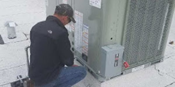 HVAC technician performing installation and maintenance on a commercial rooftop air conditioner.