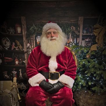 Santa Claus sitting with hands clasped, surrounded by Christmas decor.