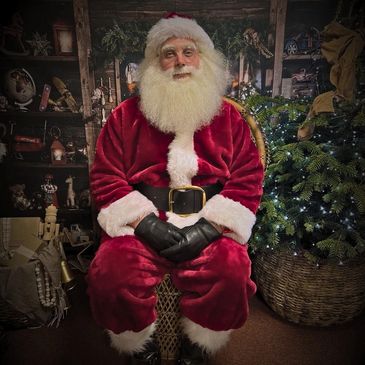 Santa Claus sitting with hands clasped, surrounded by Christmas decor.