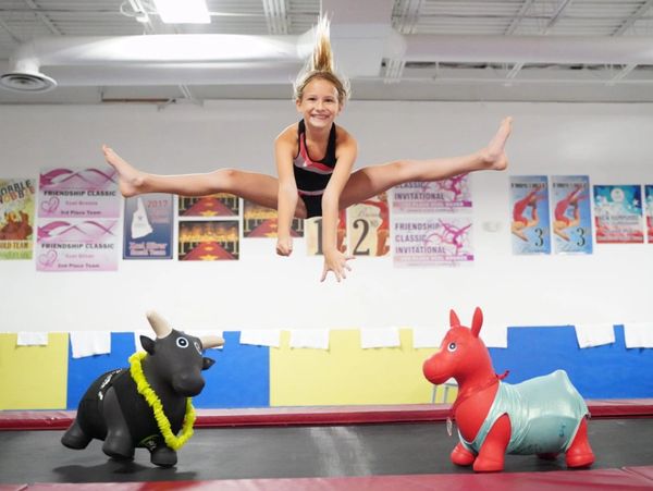 Girl jumping in a gym over inflatable toys.