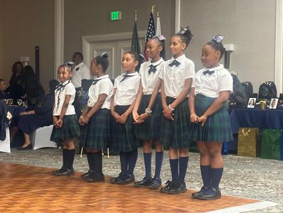 Six girls in school uniforms standing in a line indoors.