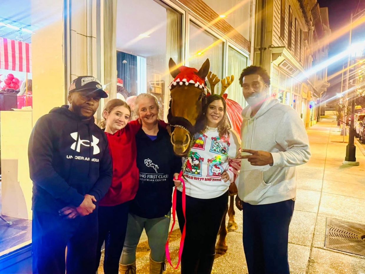 Group of five people posing with a horse on a city sidewalk at night.