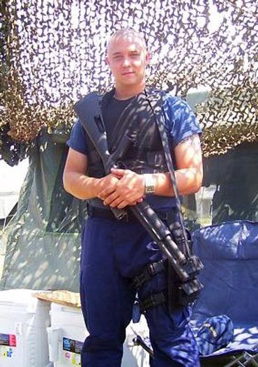 A soldier stands in front of camouflage netting holding a rifle.