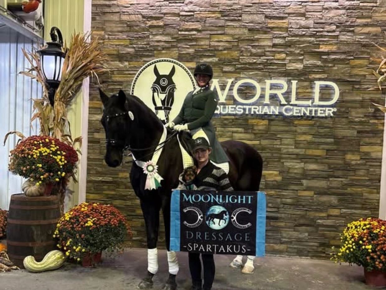 Equestrian champion posing with horse and banner indoors.