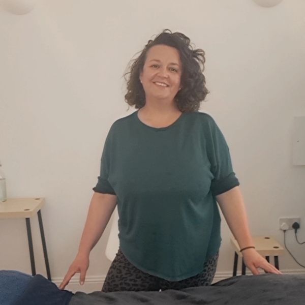 Morganne stands behind a sports massage bed in a cozy, minimalist room.