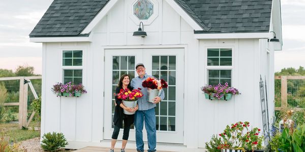 Happy couple holding flowers in front of a white farmhouse.