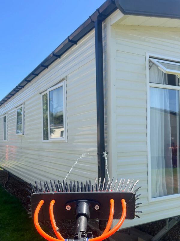 A brush attached to a hose sprays water near a mobile home on a sunny day.