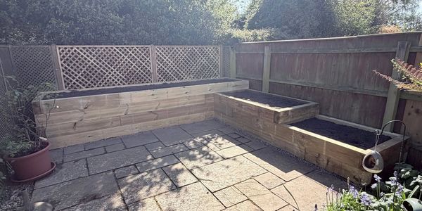 Newly built wooden garden planters and seating area on a stone patio.