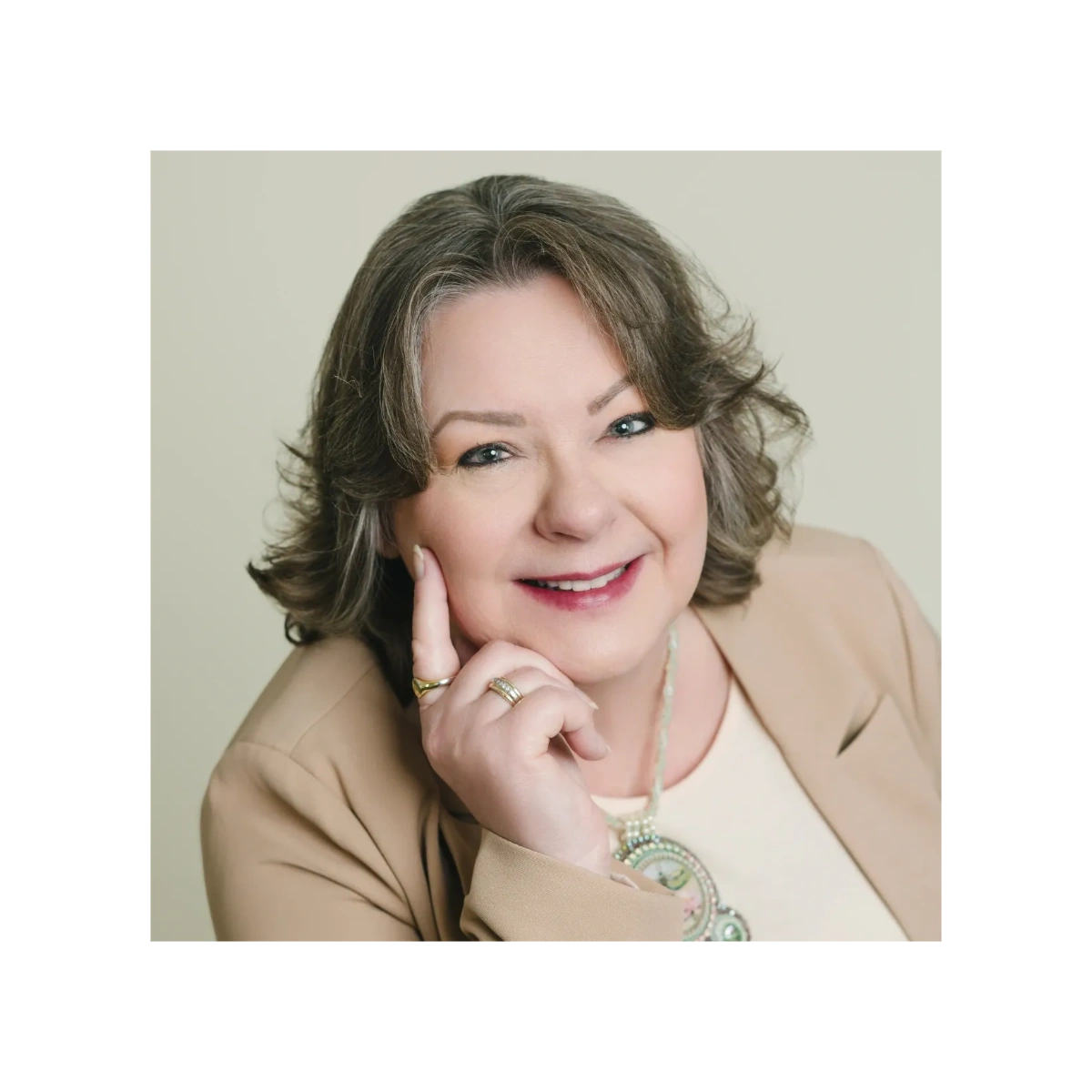 Smiling middle-aged woman with gray hair, wearing a beige blazer and a beaded necklace.