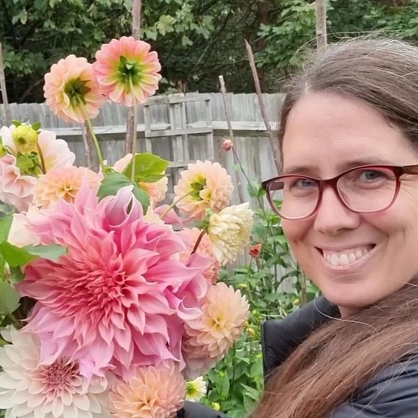 Smiling woman with glasses holding a bouquet of pink and peach flowers.