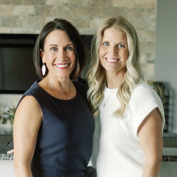 Two smiling women standing indoors.