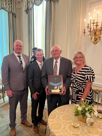 Family portrait at a formal event with an older man holding a framed photo.