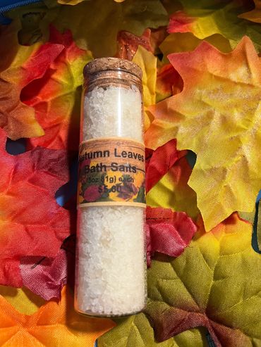 A glass vial of Autumn Leaves Bath Salts on colorful fabric leaves.