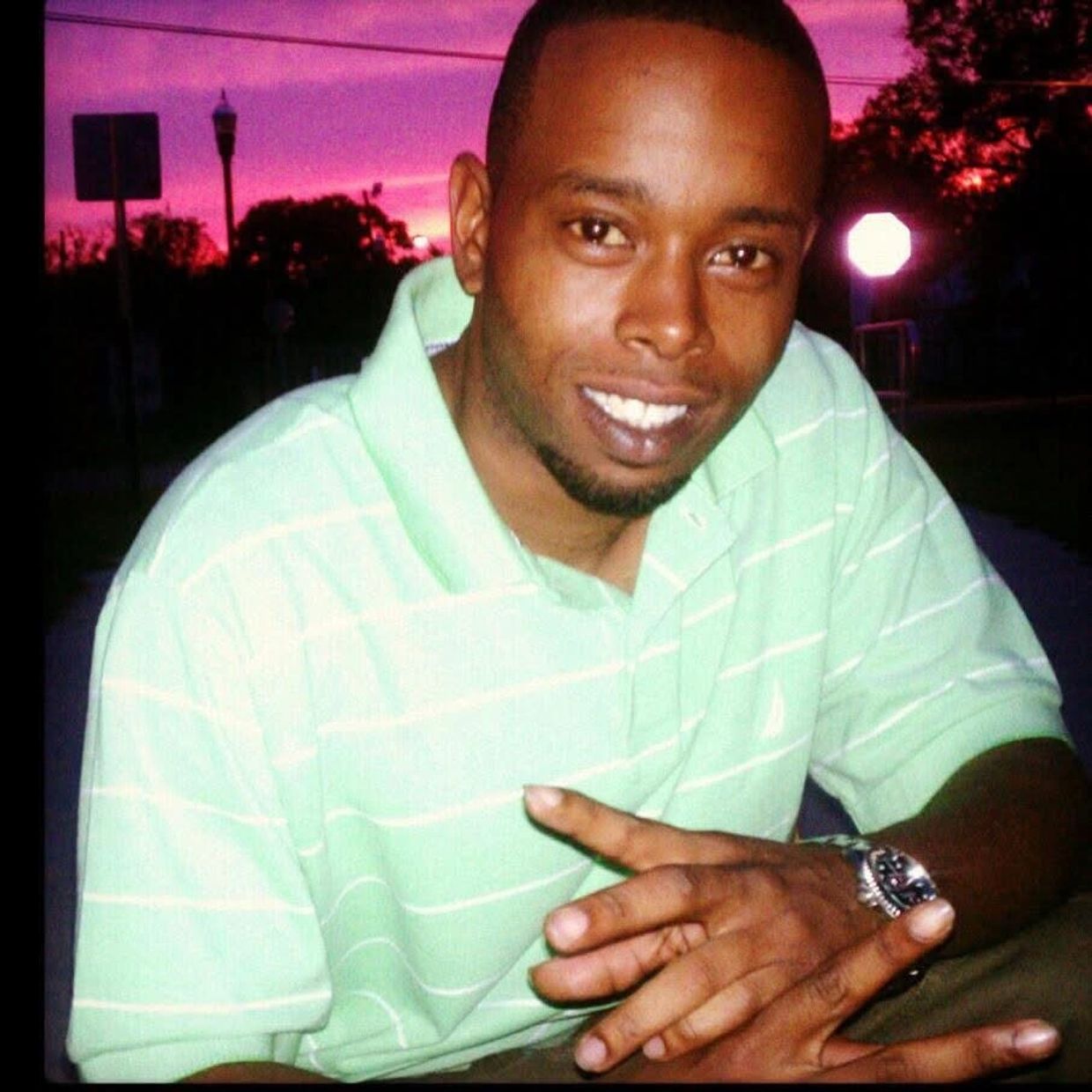 A man in a light green striped polo shirt smiles at the camera during sunset.