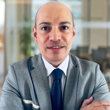 A confident businessman in a grey suit with arms crossed, smiling at the camera.
