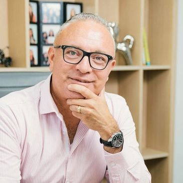 Middle-aged man with glasses and watch, sitting thoughtfully in an office.