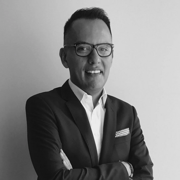 Professional man in suit with glasses, smiling confidently with arms crossed.