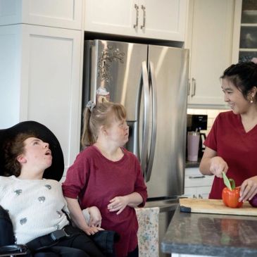 Woman and two people with disabilities preparing food together in kitchen.