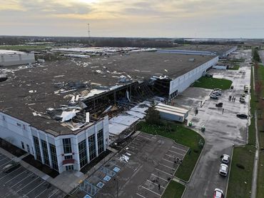 Aerial view of tornado-damaged warehouse with collapsed roof and scattered debris.