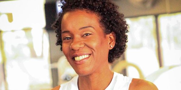 Smiling woman with curly hair wearing a white sleeveless top indoors.