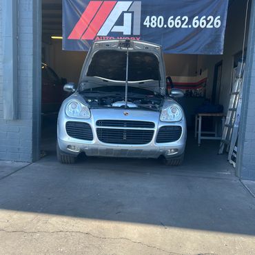 Silver Porsche with open hood in an auto repair garage.